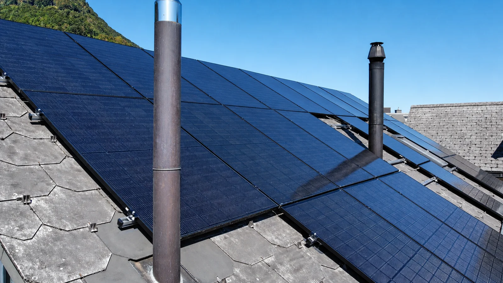 Moduli fotovoltaici neri su tetto in ardesia tra due camini